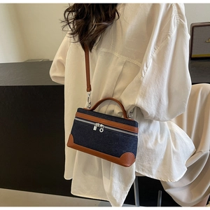 Detail of denim patchwork crossbody bag with brown leather trim worn on white shirt