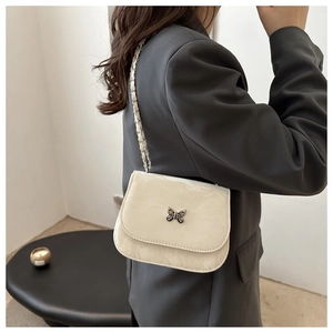 Detail of butterfly buckle and metal chain strap on cream marble textured crossbody bag