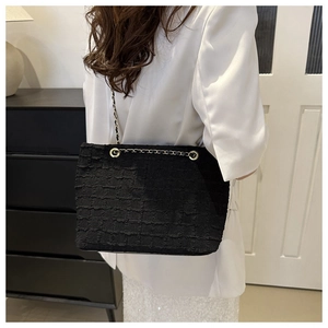 Détail du sac cabas noir texturé avec chaîne dorée porté sur un tailleur blanc