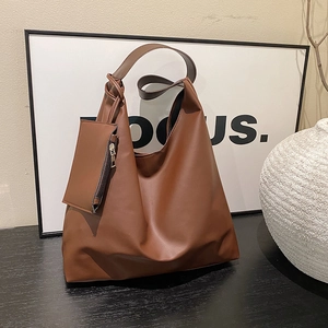 Brown minimalist leather tote bag with wide strap and matching coin purse on wood surface