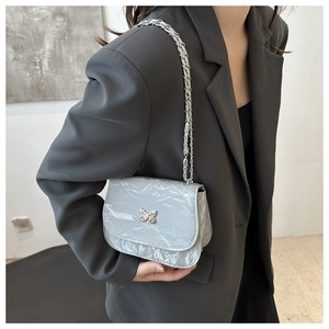 Detail of silver textured crossbody bag featuring a metallic butterfly clasp and chain strap