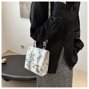 Detail view of white crossbody bag featuring black butterfly prints and dual metal buckles
