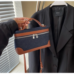 Detail of denim and brown leather patchwork crossbody bag with silver hardware and top handle