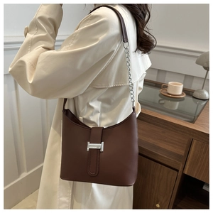 Detail of dark brown leather handbag with silver H buckle worn with beige trench coat