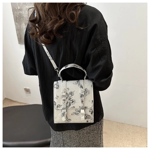 Detail of white crossbody bag featuring butterfly prints and metallic buckle on leather