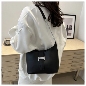 Detail of black matte leather shoulder bag with silver buckle and chain on white sweatshirt