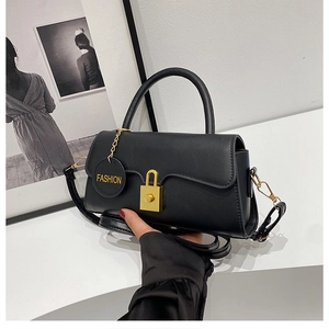 Detail of matte black crossbody bag with gold square buckle and fashion charm pendant