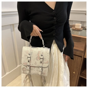 Close-up of a cream-colored handbag featuring pink butterfly prints and metal buckles
