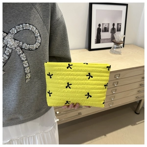Détail d'une pochette matelassée jaune avec broderies de nœuds noirs portée à la main