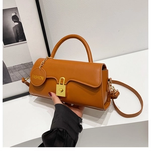 Detail of caramel crossbody bag featuring a golden lock closure and fashion charm