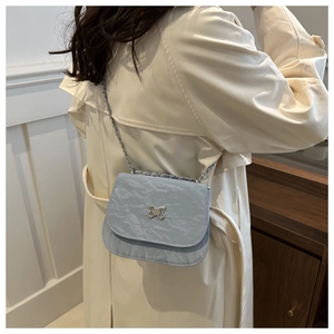 Detail of light blue pleated crossbody bag with silver butterfly buckle on beige trench coat