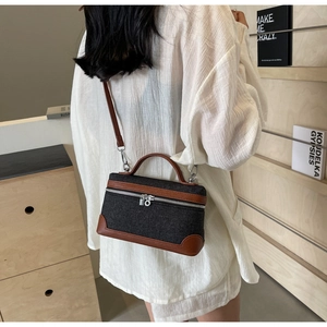 Detail of dark denim crossbody bag with brown leather trim worn by a model