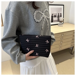 Detail of black quilted makeup bag featuring pink butterfly embroidery held by a model