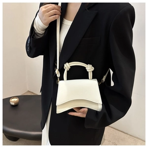 Close-up of a white leather mini handbag with a curved base and knotted handle on a model