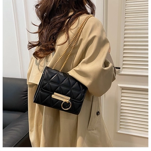 Detail of black quilted chain bag with gold ring buckle worn by a model in interior