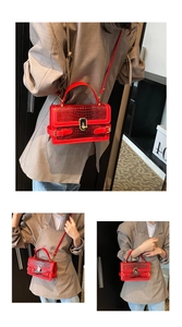 Detail of red crocodile pattern handbag with gold hardware lock and crossbody strap