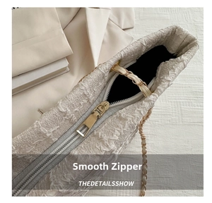 Gros plan sur la fermeture éclair dorée et la texture tweed d'un sac beige chic