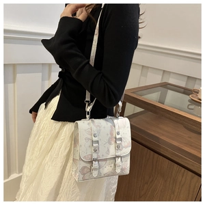 Detail of white shoulder bag featuring elegant butterfly print and silver buckle straps