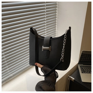Detail of a black leather underarm bag with silver H-buckle and metal chain strap