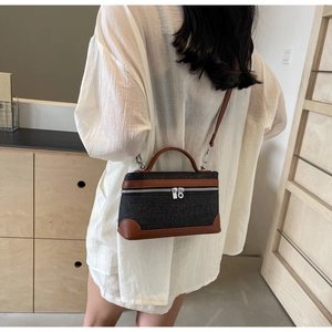 Detail of grey denim crossbody box bag with brown leather trim worn by model
