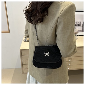 Model wearing black quilted crossbody bag with silver butterfly clasp and chain strap