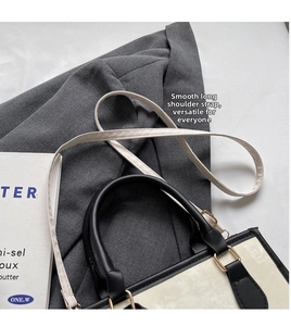 Dettaglio di una borsa tote crema chic con finiture in pelle nera su un blazer grigio