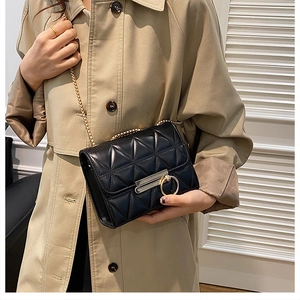 Detail of black quilted leather shoulder bag with gold chain strap on beige trench coat