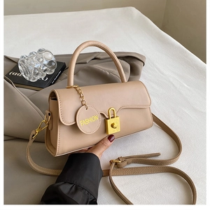 Detail of beige crossbody bag with golden square lock and fashion charm on white fabric