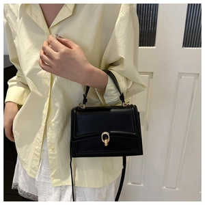 Dettaglio di una piccola borsa a tracolla nera con elegante chiusura ovale dorata