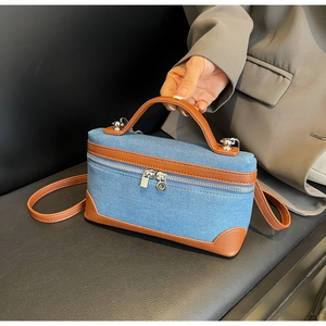 Detail of blue denim crossbody bag with brown leather trim and silver zipper hardware