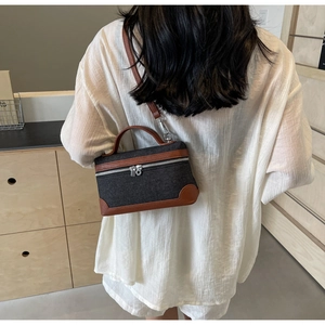Detail of gray denim small vanity case bag with brown leather trim and silver zipper