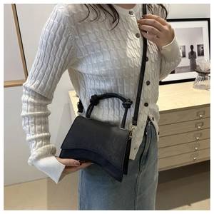 Detail of minimalist black hourglass handbag with knotted handle and curved base design