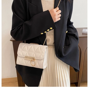 Detail view of a white quilted crossbody bag with gold chain strap and ring closure