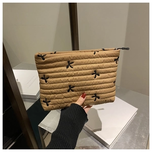 Détail de la pochette en velours côtelé matelassé beige avec nœuds brodés et fermeture éclair