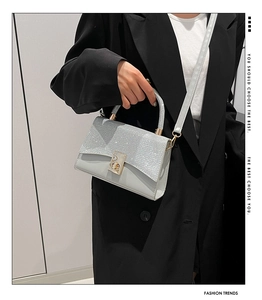 Detail of glitter flap texture and gold twist lock on light grey crossbody bag