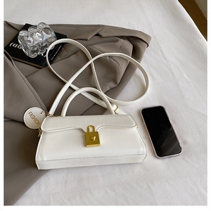 White faux leather crossbody bag with golden square lock and fashion charm on a desk
