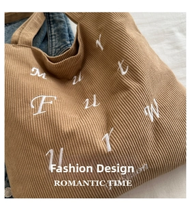 Detailed texture of brown corduroy tote bag with white letter embroidery and fabric finish