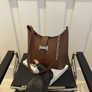 Brown leather underarm bag with silver H-buckle and metal chain on a black leather chair
