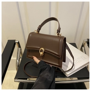 Dettaglio borsa quadrata in finta pelle marrone scuro con fibbia dorata su sedia nera