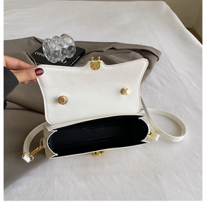 Detail view of white faux leather crossbody bag with gold hardware and black fabric lining