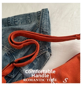 Close-up of orange corduroy tote bag with white S letter detail on blue denim jacket