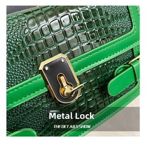 Macro view of green crocodile pattern leather and gold hardware lock on crossbody bag