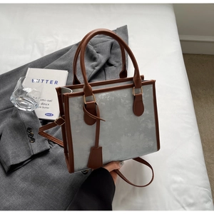 Close-up of a grey stone-textured tote bag with brown leather handles on a white bed
