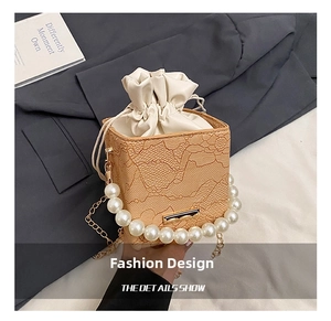 Detail of beige lace textured bucket bag with pearl handle and golden chain on grey fabric