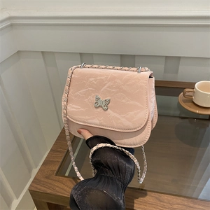 Pink saddle crossbody bag with metal butterfly detail and chain strap in cafe setting