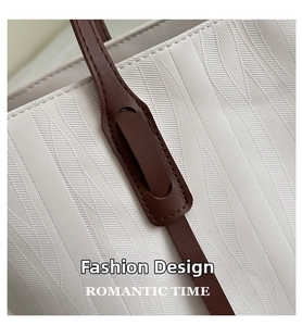 Close-up of white leather tote with diagonal herringbone texture and brown handle