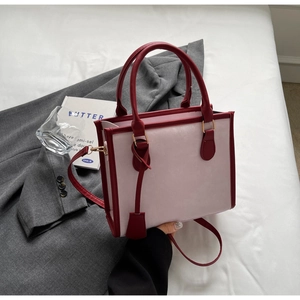 Detail of contrast color tote bag with dual handles and gold-tone hardware on grey blazer