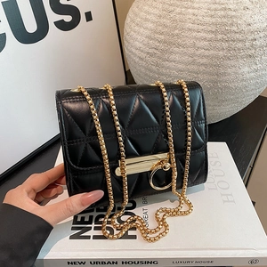 Glossy black quilted shoulder bag with gold chain and circular lock on white books