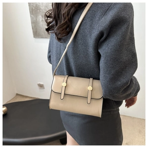 Detail view of a beige crossbody bag with decorative straps and golden hardware on a model