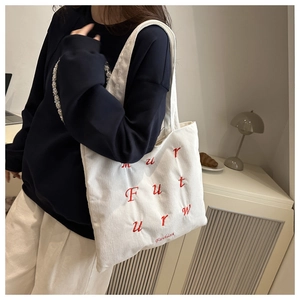 Detail of white corduroy tote bag with red letter embroidery worn by model in home setting